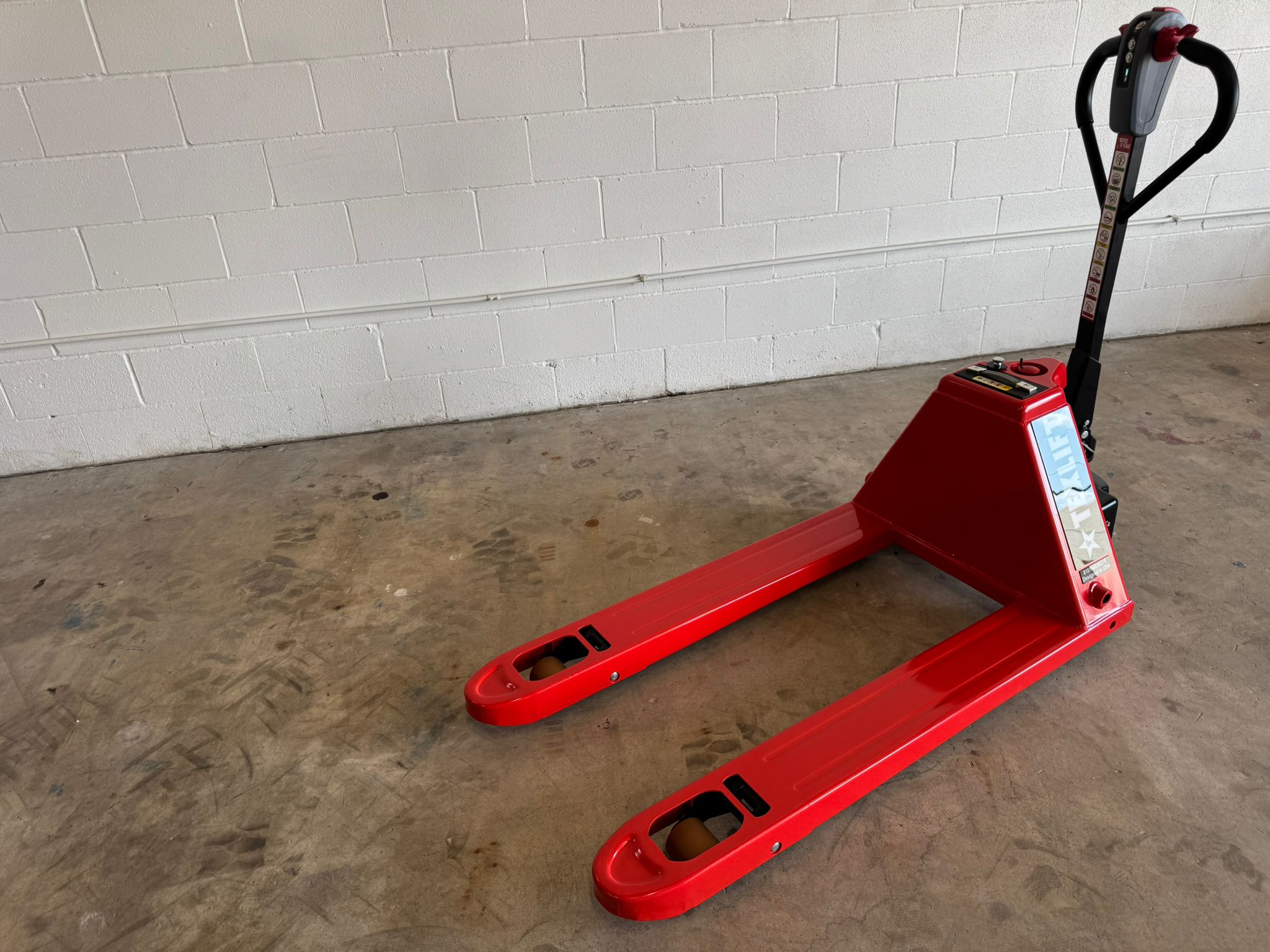 Red pallet jack on a concrete floor with a white brick wall in the background